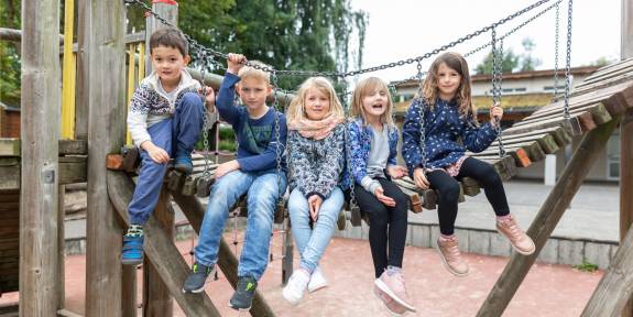 Mehrere Kinder sitzen gemeinsam auf der Hängebrücke der beiden Spielhäuser